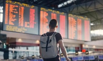 A man with a backpack looking at a departure and arrival schedule board in an airport.
