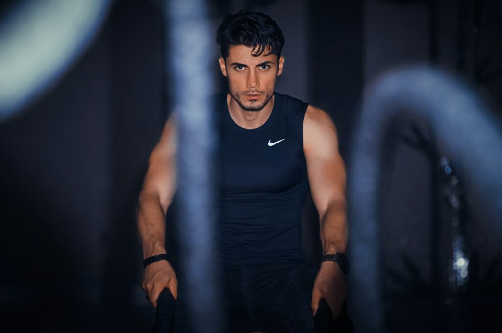 Focused man training with battle ropes in a gym, building strength and stamina during a pre vacation workout routine.