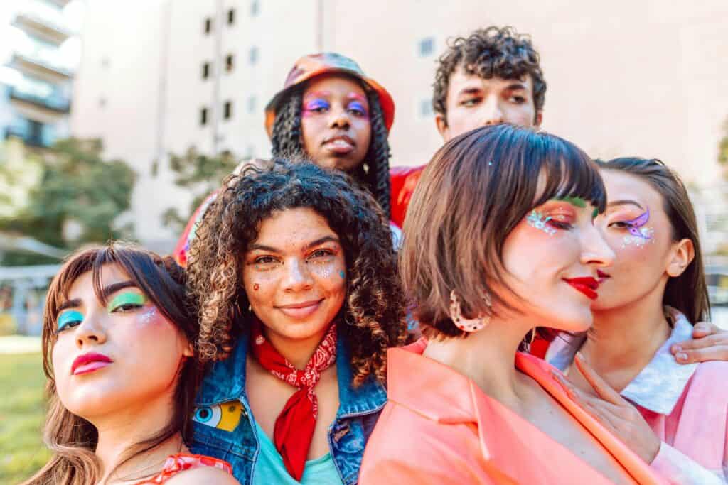Group of diverse friends with colorful makeup and glitter at a pride event, celebrating the Gay Travel Generational Gap.