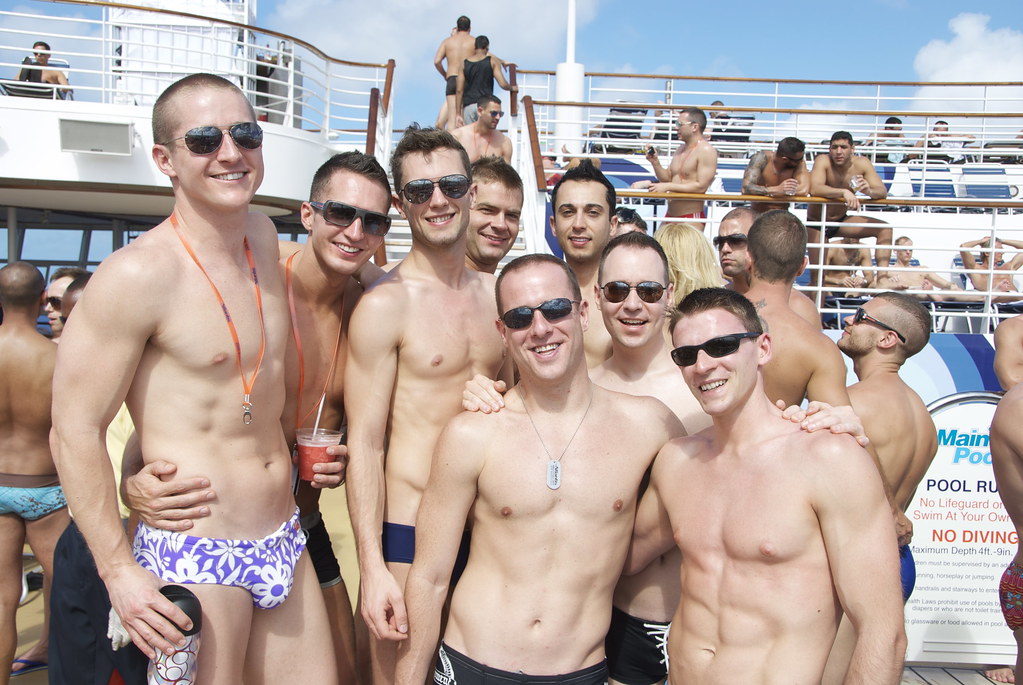 Group of shirtless men posing on a cruise ship deck during a sunny pool party — showcasing cheap gay travel with friends at sea.