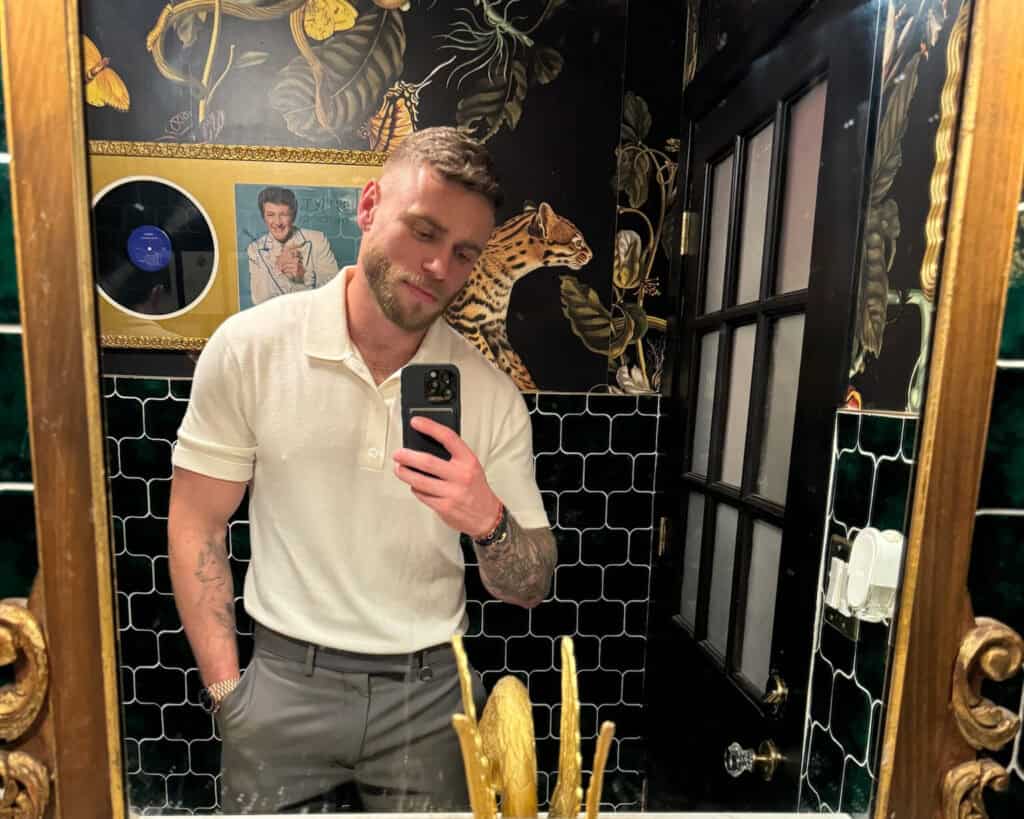 Gus Kenworthy taking a mirror selfie inside Little Gay Pub gay bar in Washington, DC, featuring bold wallpaper and eclectic décor.