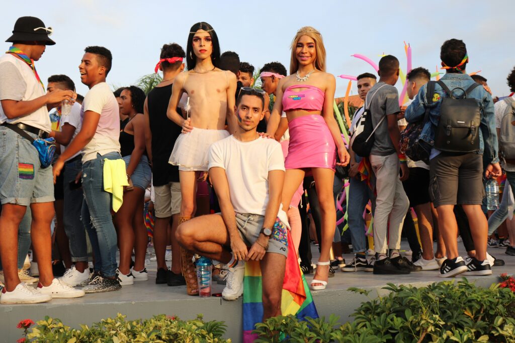 LGBTQ+ crowd celebrating at an outdoor festival with rainbow flags and bold fashion, highlighting cheap gay travel through Pride events.