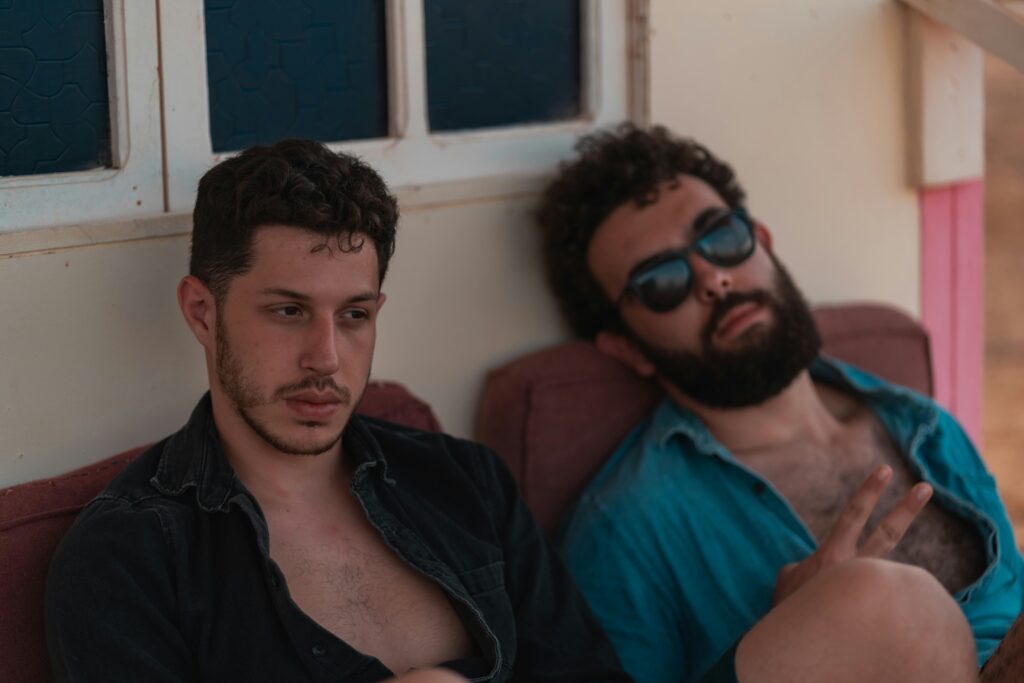 Two men lounging together in casual outfits, relaxing during an affordable getaway — cheap gay travel downtime.