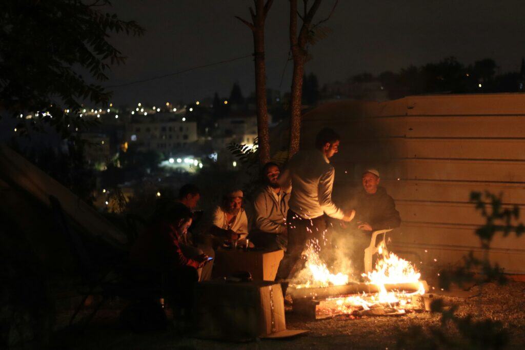 Friends gathered outdoors by a fire at night, celebrating togetherness and reflection tied to gay travel Jewish holidays.