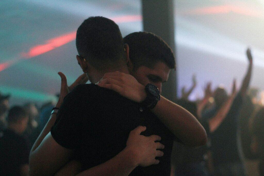 Two men embracing closely in a crowded venue, reflecting themes of connection and renewal during gay travel Jewish holidays.