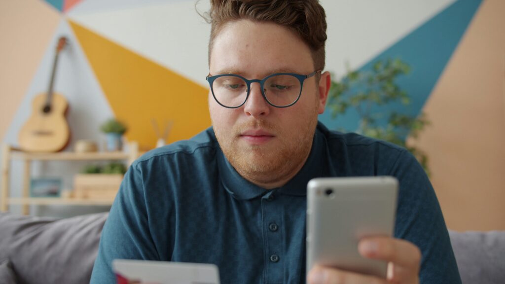 Traveler holding a credit card and smartphone, researching flight deals online — smart planning for cheap gay travel.