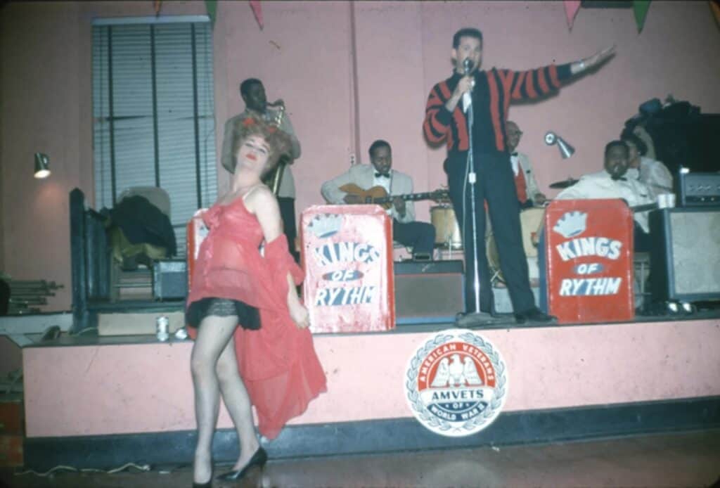 Vintage photo of a drag queen performing with a live band in Kansas City, reflecting queer culture’s resilience.
