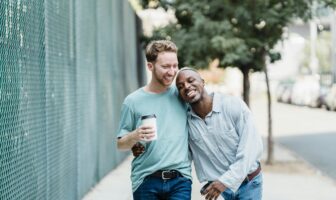 Two men walking arm in arm through a city neighborhood, a relaxed moment that reflects slower gay travel ideas 2026 focused on connection over spectacle.