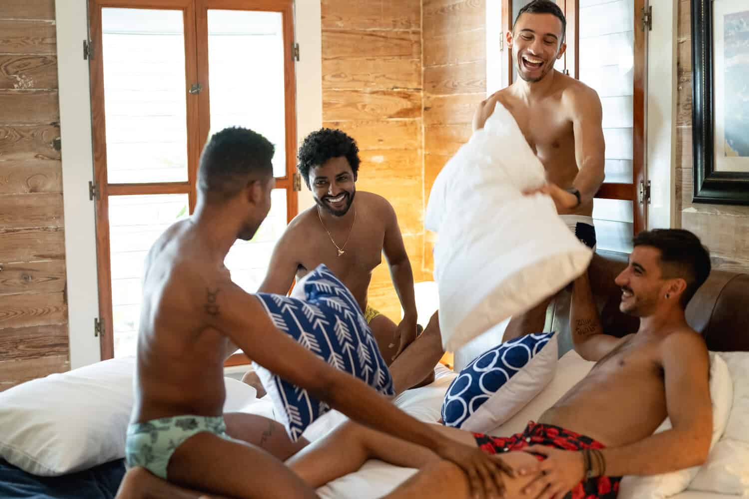 Group of men laughing together on a bed, showing the playful and social side of gay travel intimacy in shared spaces