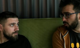 Two men sitting close and talking on a couch, sharing an intimate conversation in a relaxed indoor setting