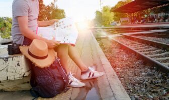 Traveler waiting at a train platform with a map and backpack, illustrating how gay travel trends 2026 favor timing and flexibility
