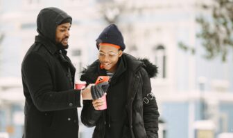 Two men bundled up in winter coats checking a phone together outdoors, planning gay Valentine’s Day travel during a cold city break.