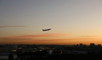 Airplane taking off at sunset over a city skyline, symbolizing modern travel volatility and flight delay compensation help.