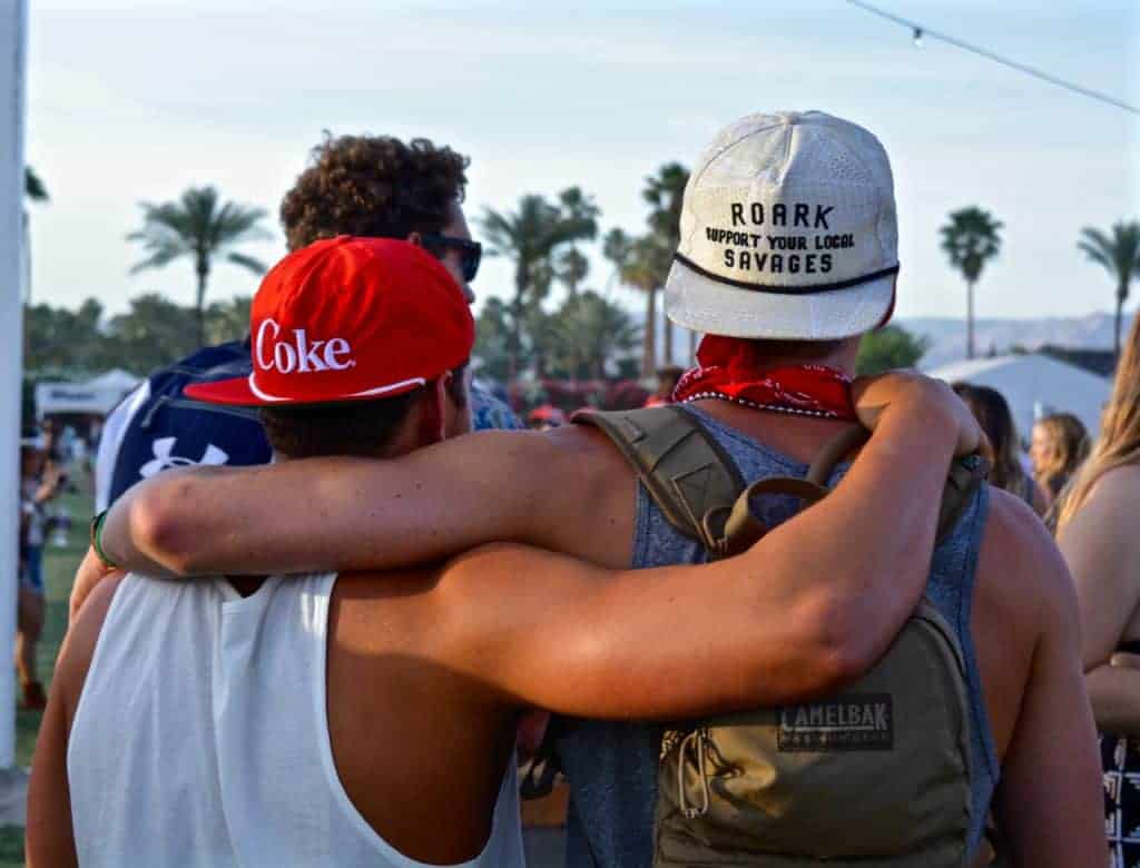 Group of friends with arms around each other at an outdoor music festival during a sunny spring day