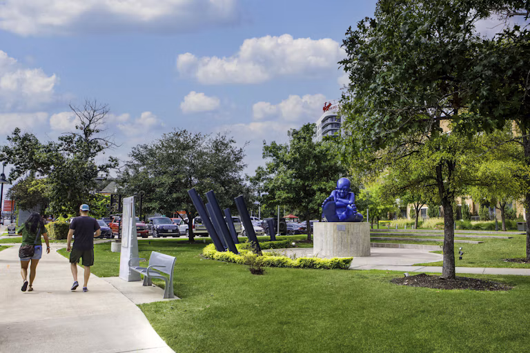 Dallas Design District park featuring outdoor sculptures, green lawns, and a pedestrian walkway.